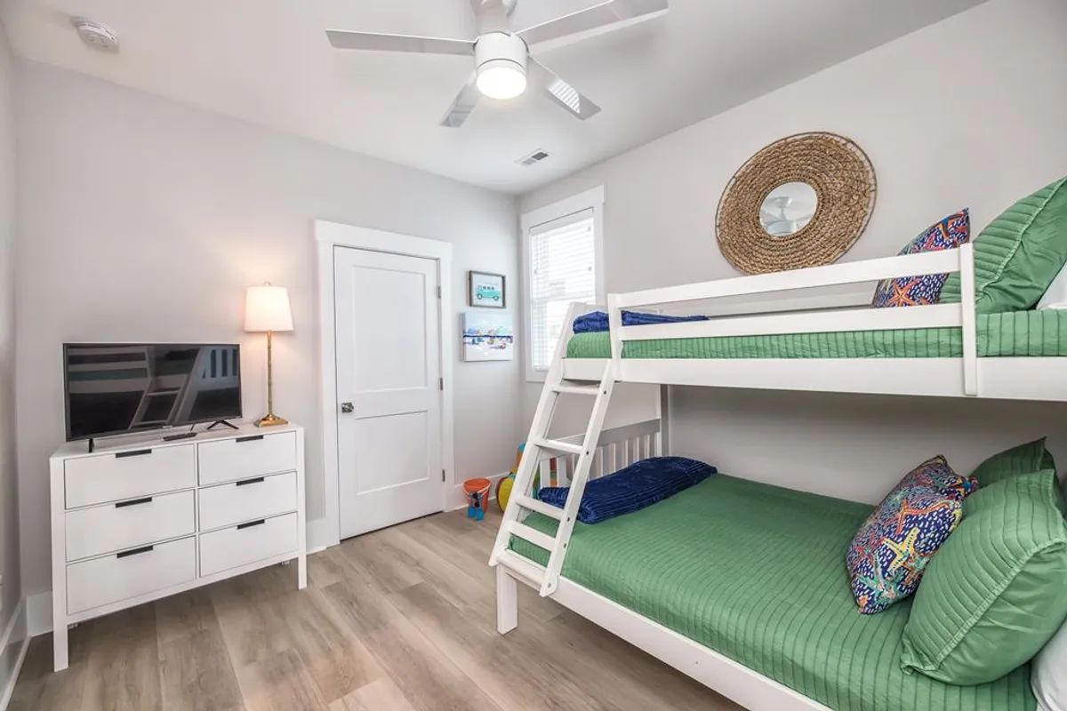 A playful bunk room with colorful pillows, a television mounted above a dresser, a decorative mirror, and cheerful accents. The space looks cozy and perfect for children or groups to enjoy movie nights and sleepovers.