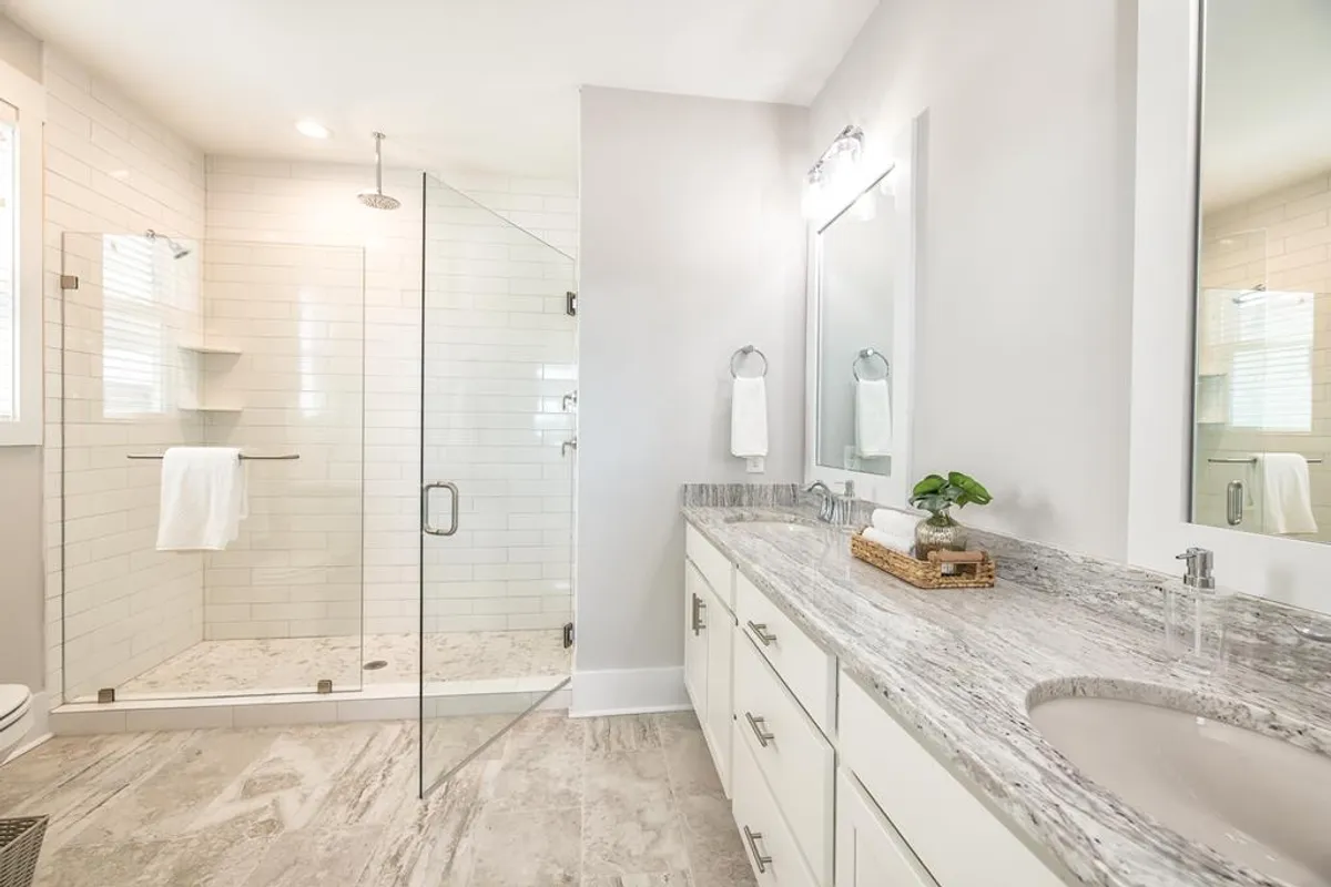 A luxurious, spa-inspired bathroom with a glass shower enclosure, double vanity, marble countertops, and natural light streaming in through a window. The overall feel is calm and rejuvenating.