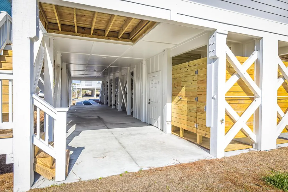 The ground-level area showcases wooden storage units, white railings, and a concrete floor—ideal for stowing beach gear, leashes, or pet supplies. The open, accessible design hints at ease of access for outings and a community feel with close neighbors.
