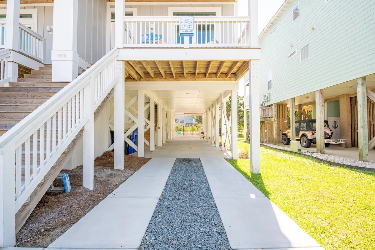An inviting exterior view shows a covered walkway and stairs leading up to the home’s entrance, set against a well-kept green lawn. The welcoming layout is ideal for gatherings or enjoying time outdoors, perfectly embodying the inviting coastal atmosphere described in the section.