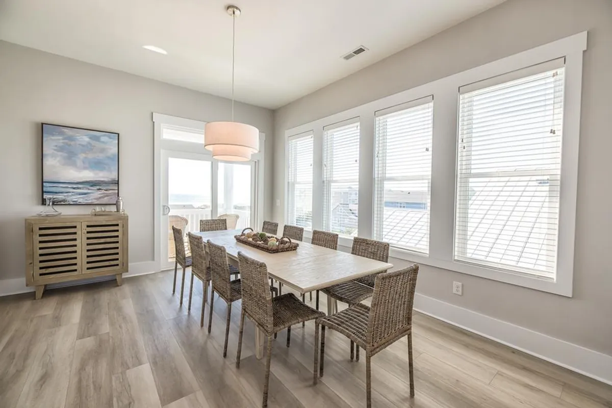 A large dining table surrounded by woven chairs sits beneath a stylish light fixture, set against a backdrop of tasteful artwork and plenty of natural light. The space is inviting and ready for family dinners or festive gatherings, comfortably accommodating a large group.