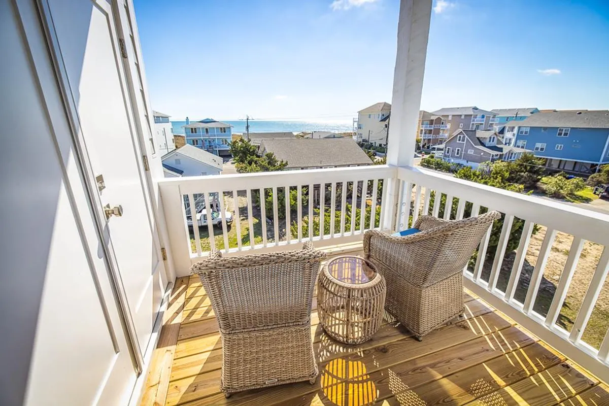 An inviting private balcony scene with wicker chairs and a small table overlooking an ocean view. The space is ideal for enjoying coffee, reading, or simply soaking in the tranquil ambiance and fresh air.