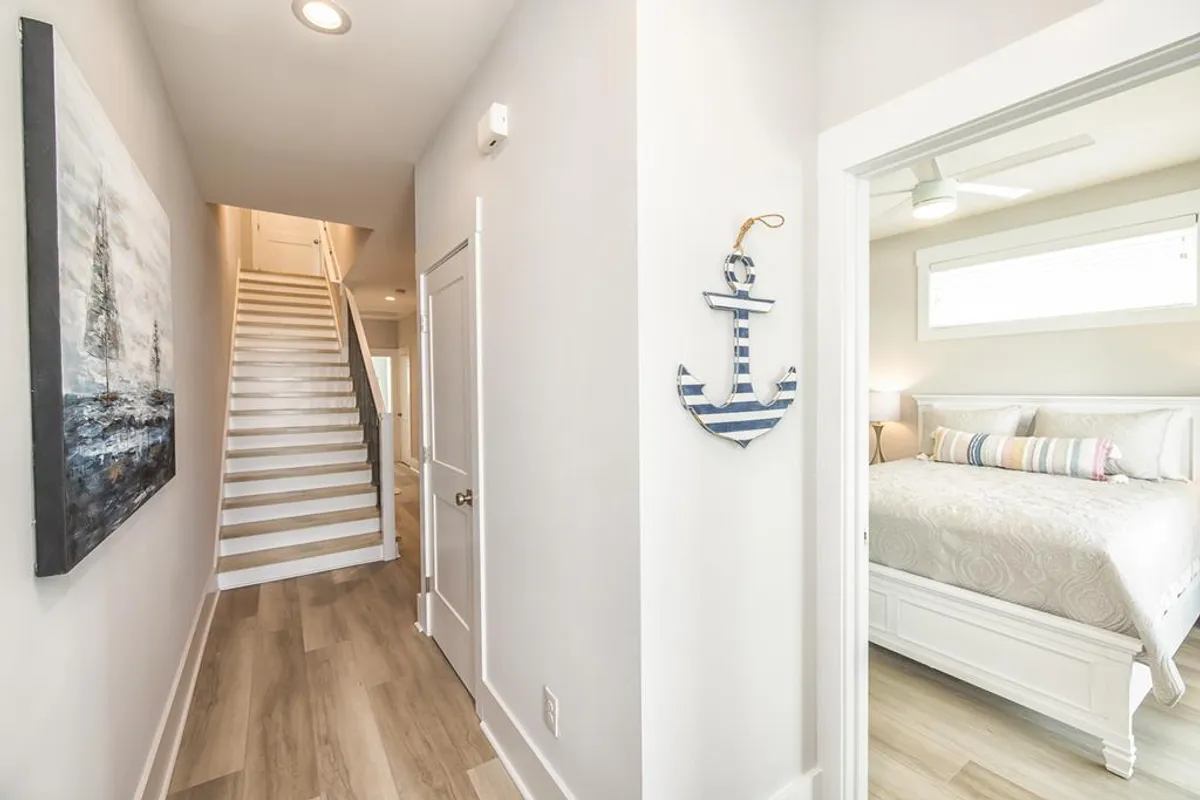 A bright hallway with a staircase, wall art, and anchor decor, leading toward the bedroom area. The scene feels peaceful yet ready to greet guests, offering a subtle nod to the area's coastal motif and the anticipation of coming home after a day of seasonal adventures.