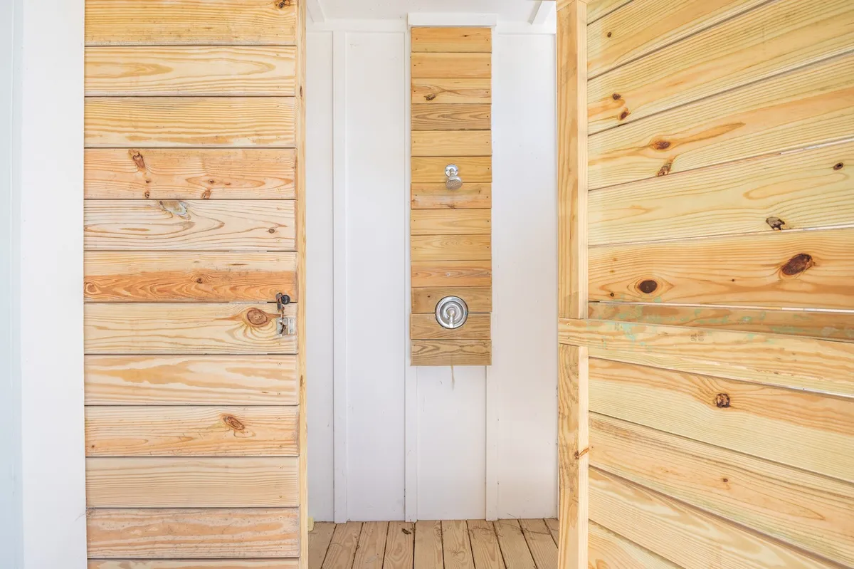 A natural, serene outdoor shower space with wooden paneling and a view of the doorway, embodying the experience of rinsing off after beach time or water activities.