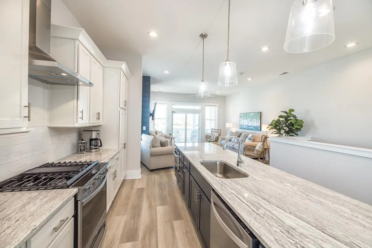 An open-concept kitchen features a granite countertop, stainless steel appliances, pendant lighting, and a view into the adjacent living area. The space is bright and inviting, designed for entertaining and casual mornings, with visual cues that it opens up toward the rest of the home and potentially outward to balconies or decks.