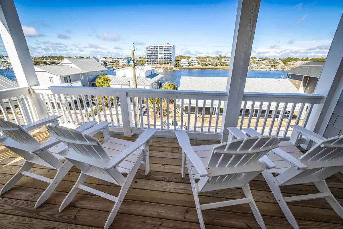 A serene deck features white Adirondack chairs facing a beautiful canal or waterfront, framed by a wooden railing. The scene is tranquil, ideal for enjoying breezes, sunsets, or stargazing—directly tying to the narrative's multiple deck experiences.