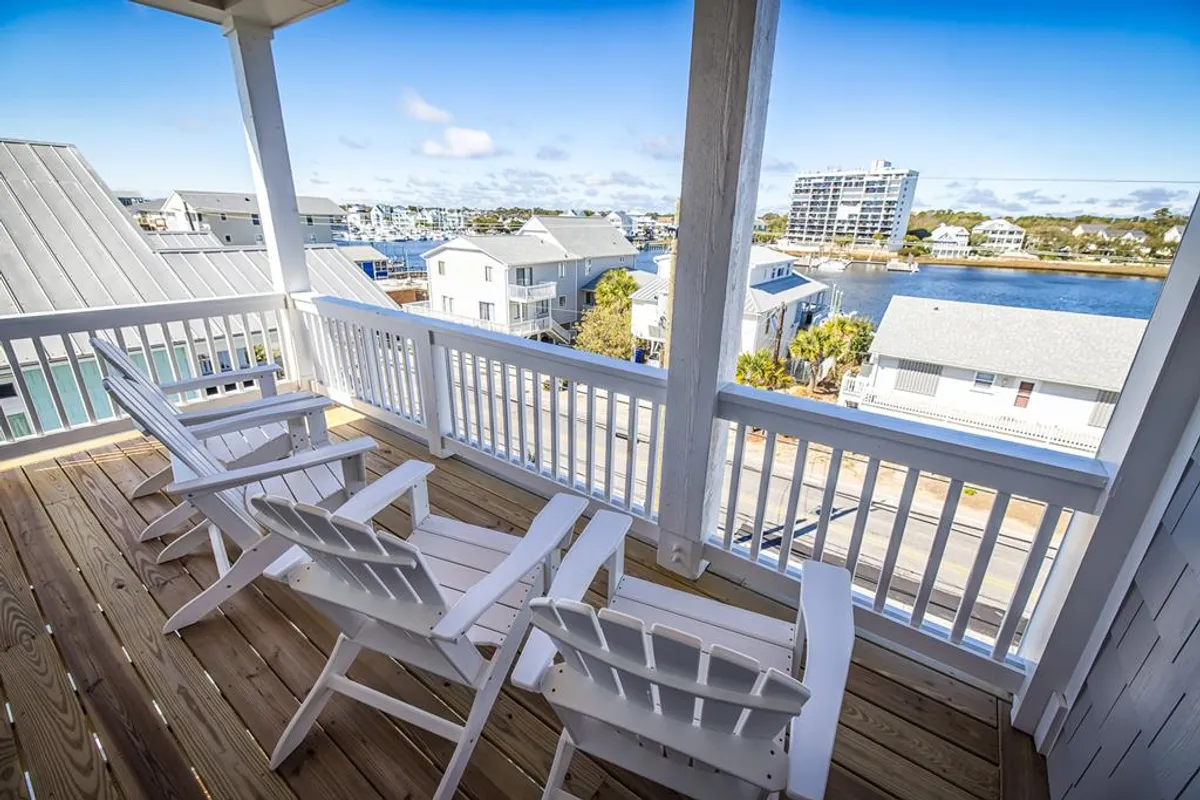 A peaceful exterior setting with Adirondack chairs overlooking a water view, surrounded by neighboring homes. The atmosphere is tranquil, emphasizing relaxation, socializing, and waterfront enjoyment.