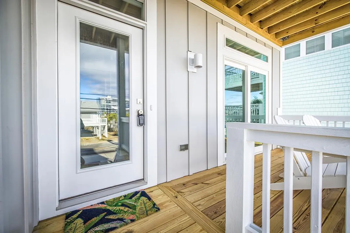 The view features a welcoming front door with deck chairs and a cheerful welcome mat, basked in natural light. The inviting setup suggests a transitional space between indoors and the great outdoors—a perfect place to pause with your pup after a walk or before heading to the beach.
